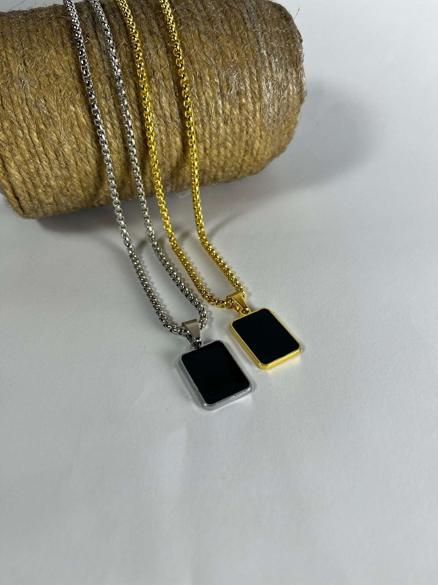 Minimalist black inlay pendant necklace in silver and gold chains on rope background.