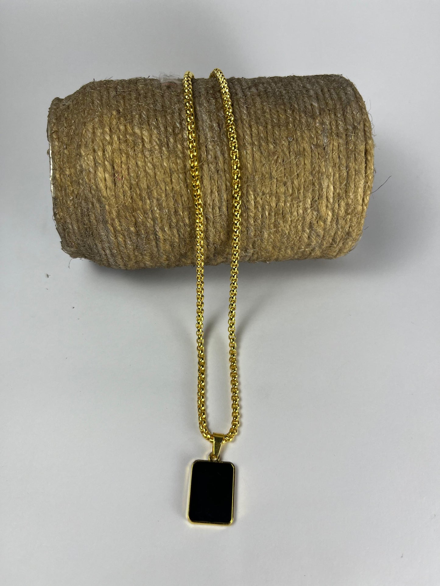 Gold chain necklace with a black pendant on a textured beige surface
