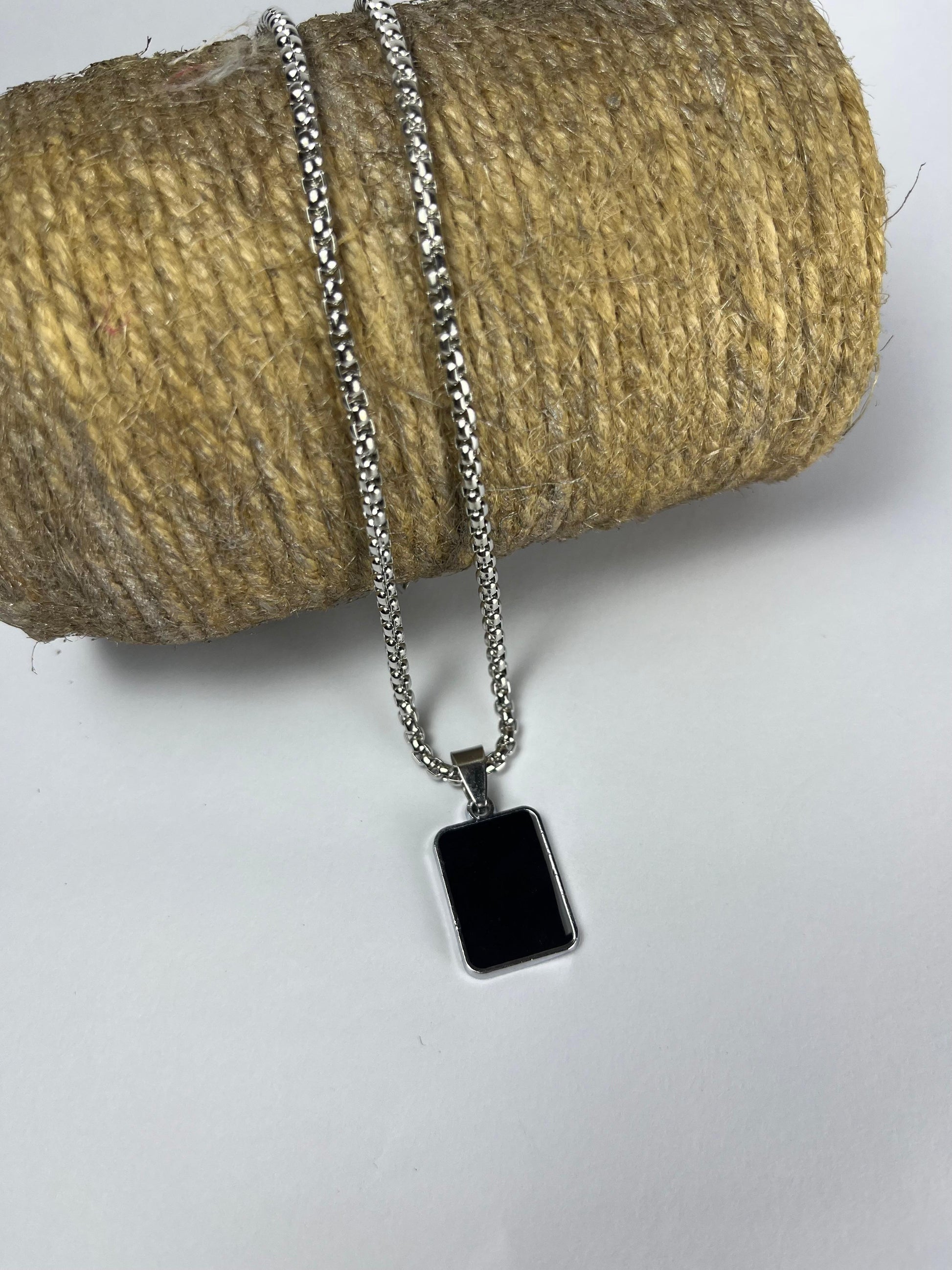 Necklace with a black square pendant on a spool of thread